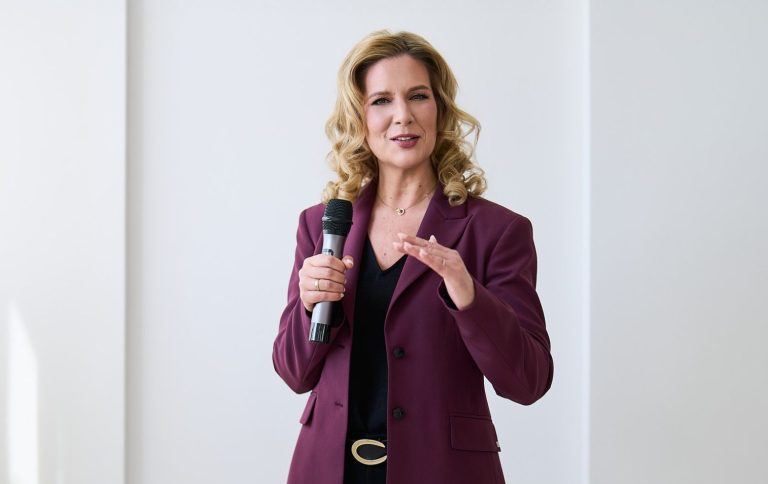 Natascha Enders – professionelle Eventmoderation Natascha Enders in lila Blazer, spricht mit einem Mikrofon in der Hand.